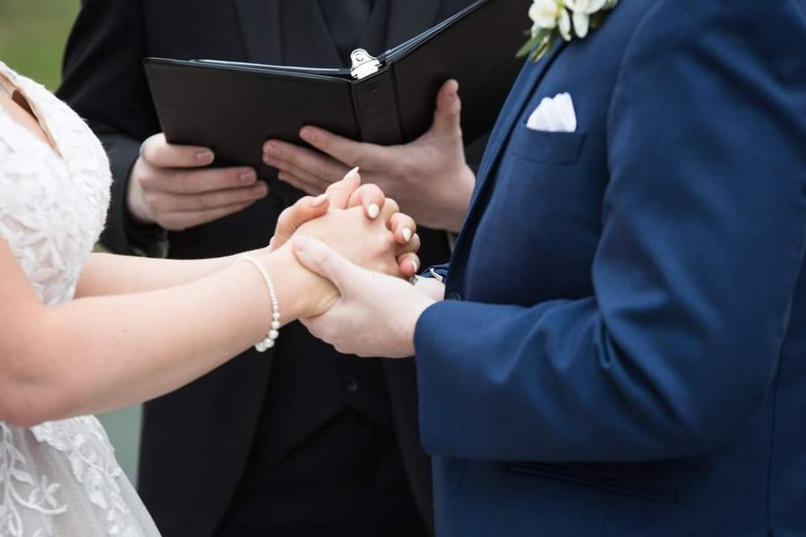 A couple holding hands while Reed reads from his ceremony book