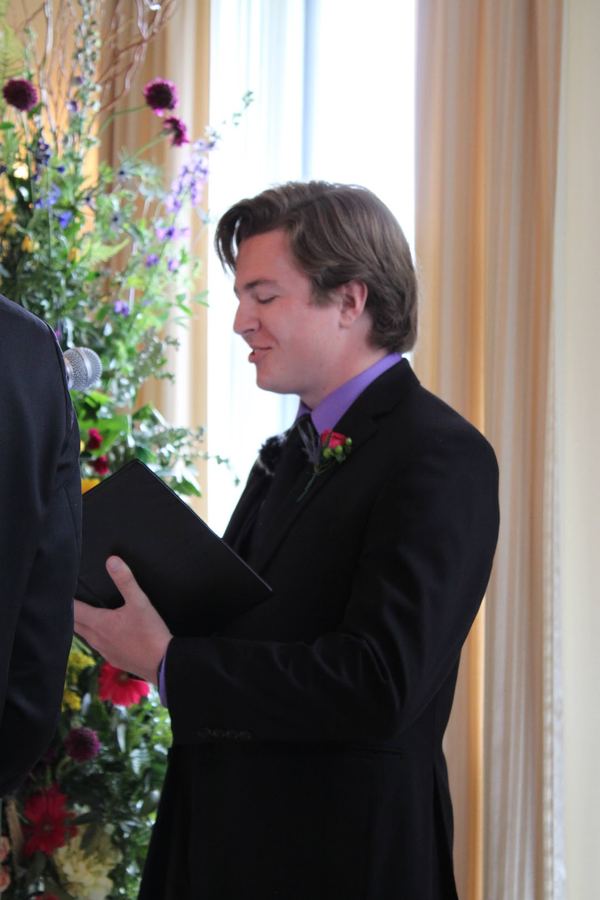 Reed reading the ceremony beside tall flowers in a sunlit room